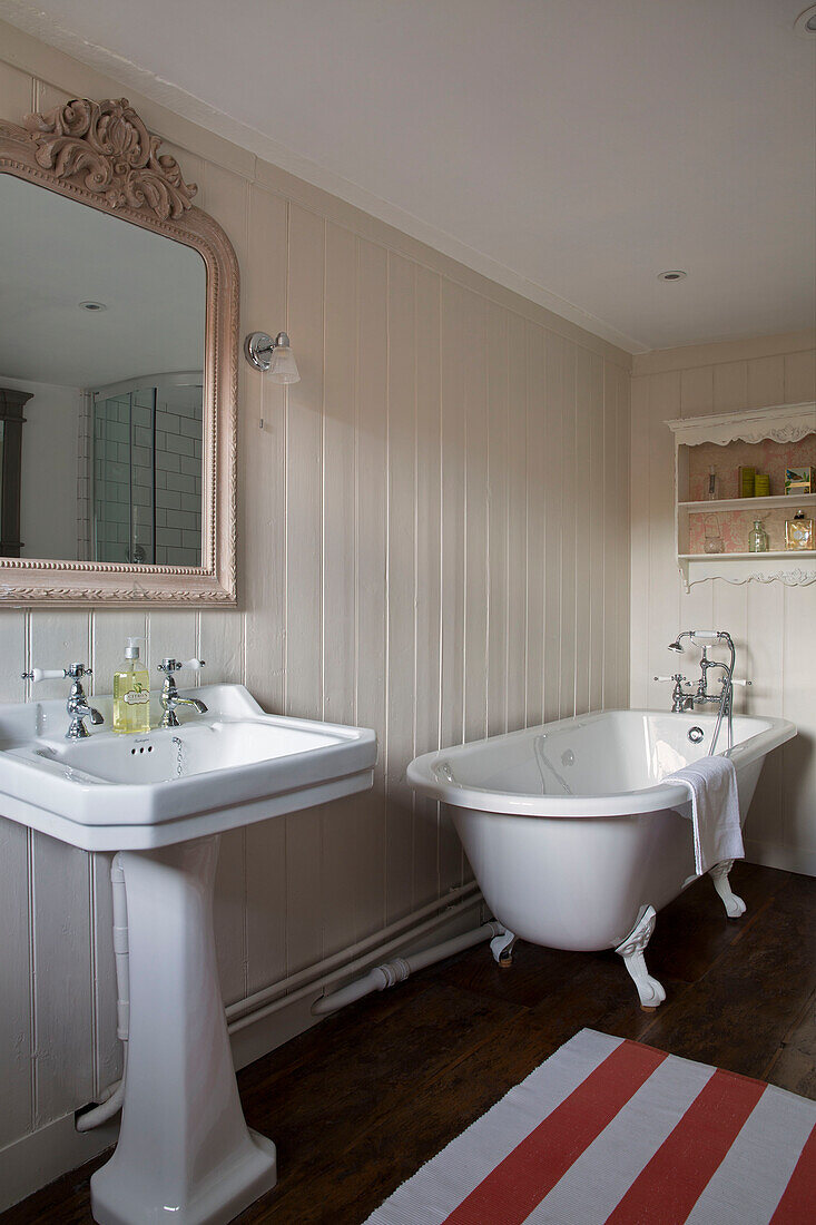 Sockelwaschbecken und freistehende Badewanne mit gestreiftem Badvorleger in einem Londoner Haus, England, UK