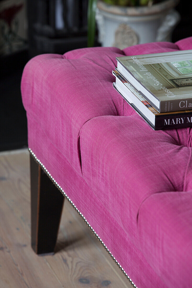 Books on bright pink buttoned ottoman in London home,  England,  UK