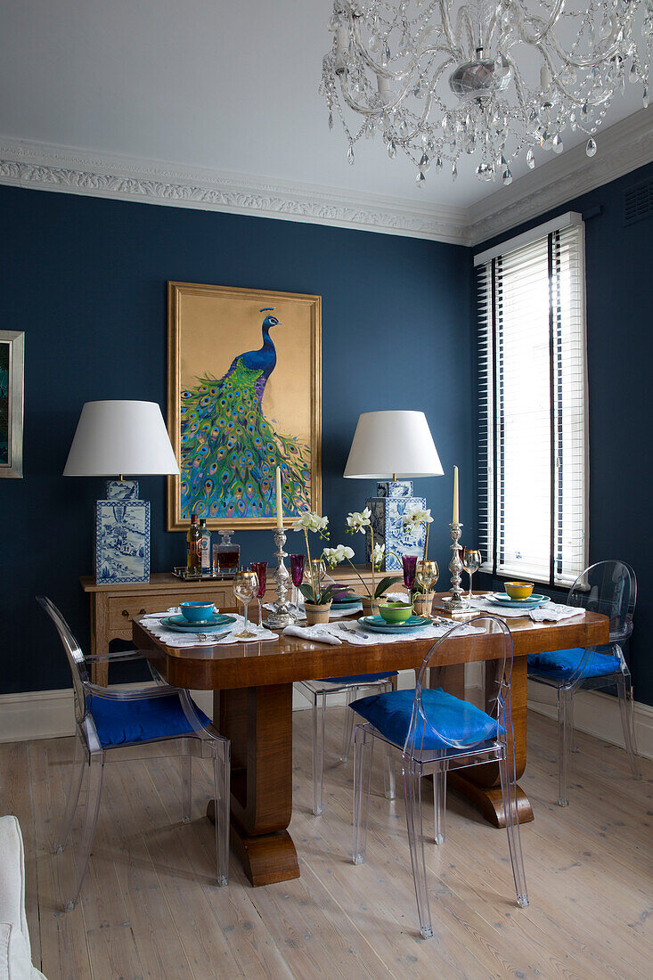 Polierter Holztisch in blauem Esszimmer mit vergoldetem Pfauen-Kunstwerk und Lampen in Londoner Wohnung, England, UK