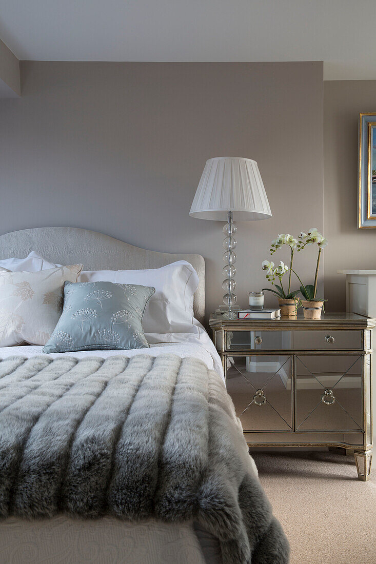 Weiße Lampe und Orchidee auf Spiegelschrank mit grauer Decke auf Bett in Londoner Wohnung, England, UK