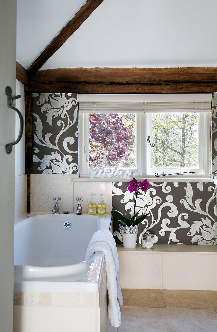 Silberne Metallic-Tapete an der Fensterumrandung mit Badewanne im Landhaus Sandhurst, Kent, England, Vereinigtes Königreich