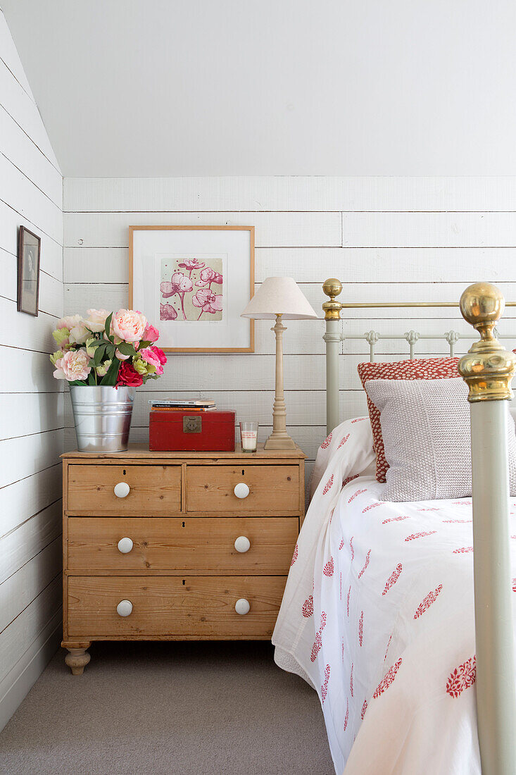 Wooden chest of drawers with cut flowers at bedside in Surrey home, England, UK