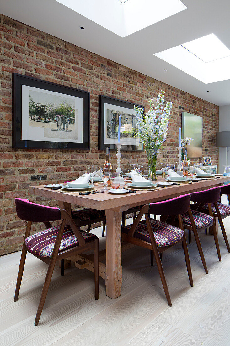 Cut flowers on dining table with retro styled chairs with exposed brick wall in London home, England, UK