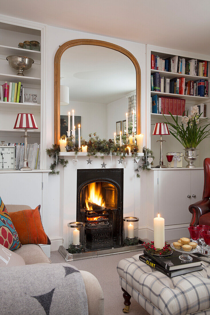Großer Spiegel über beleuchtetem Feuer mit Bücherregalen im Wohnzimmer in Surrey, England UK