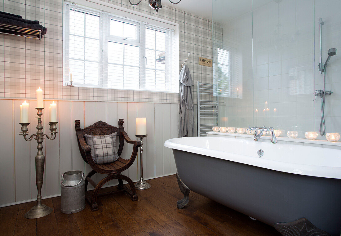 Beleuchtete Kerzen und Holzstuhl mit grauer freistehender Badewanne Surrey home England UK
