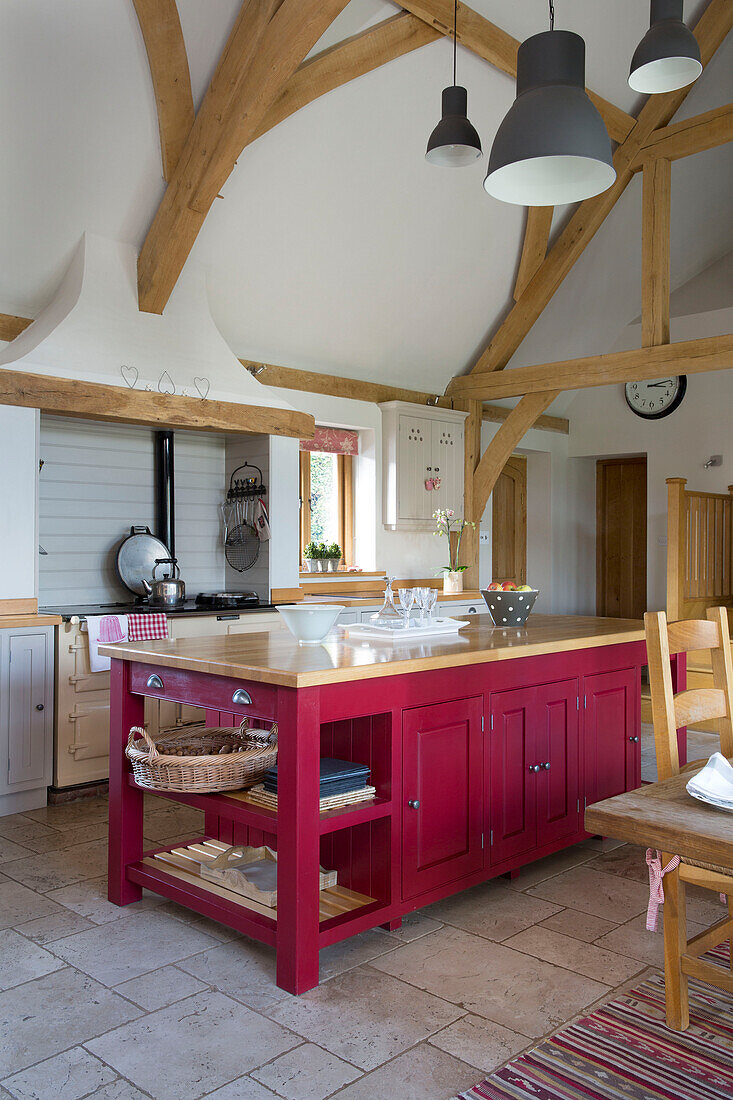 Offene Küche mit Balkendecke und roter Kochinsel in einem Bauernhaus in Sussex, England UK