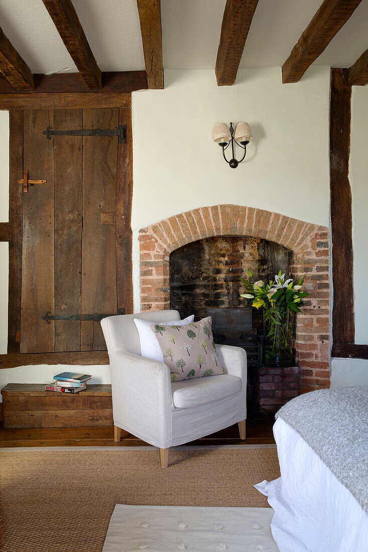 Weißer Sessel am gemauerten Kamin im Wohnzimmer eines Bauernhauses in Sussex England UK
