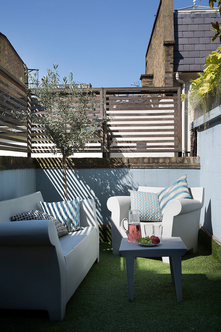 Armchair and sofa with table on astroturf in fenced backyard of London townhouse   England   UK