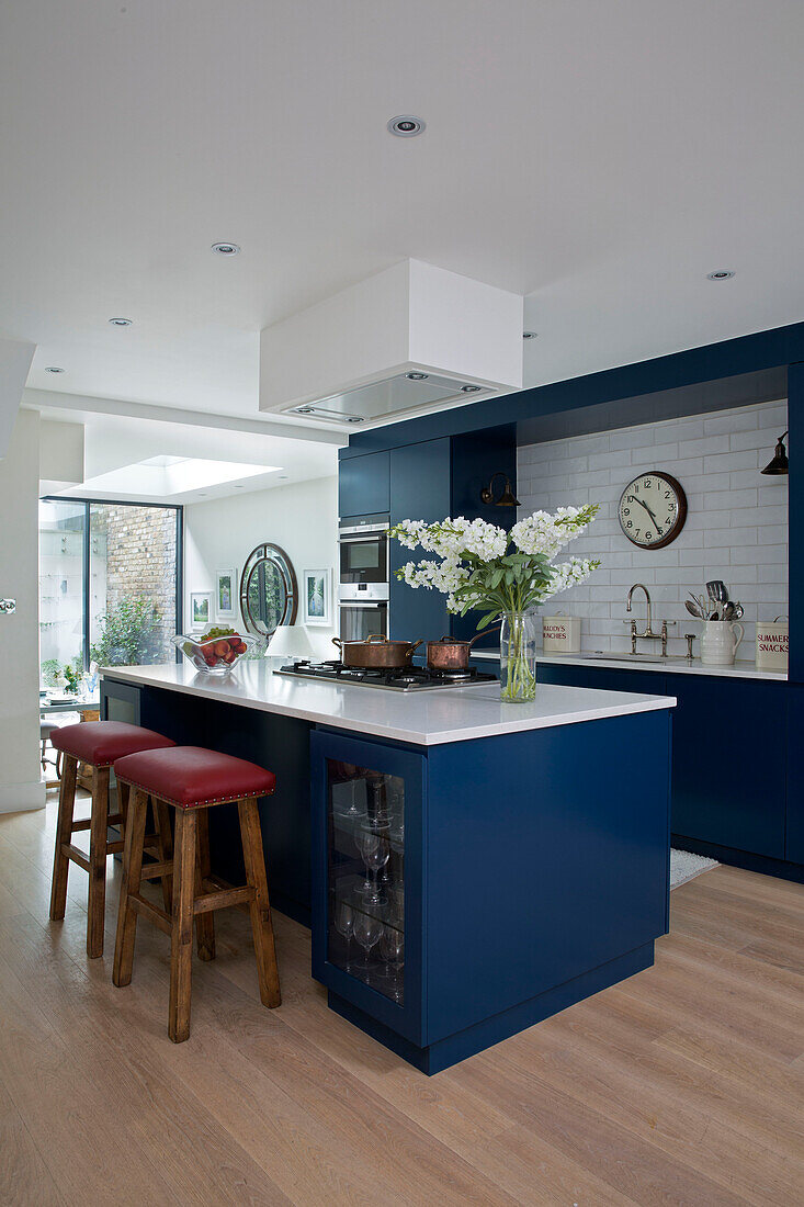 Schnittblumen auf blauer Kücheninsel mit Barhockern in der Küche eines Londoner Stadthauses, England UK