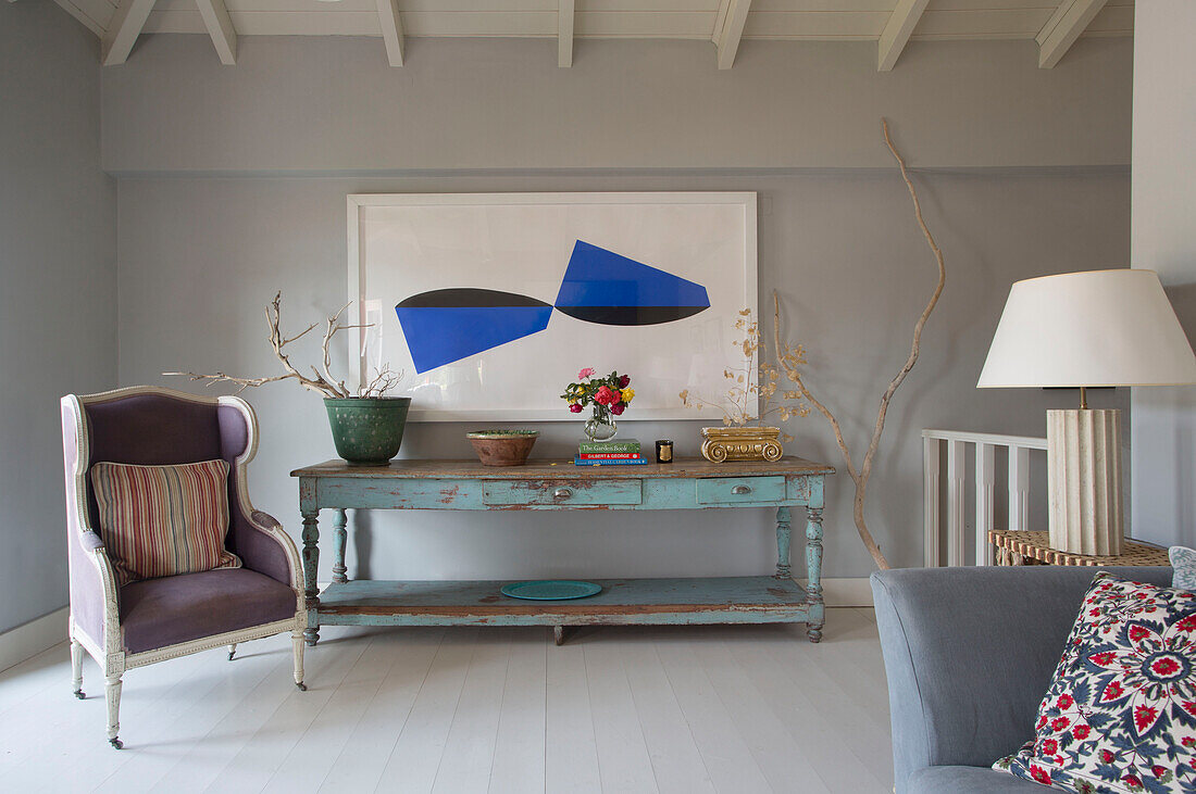 Modern artwork above wooden console with wingback armchair in 18th century Ithaca townhouse Greece