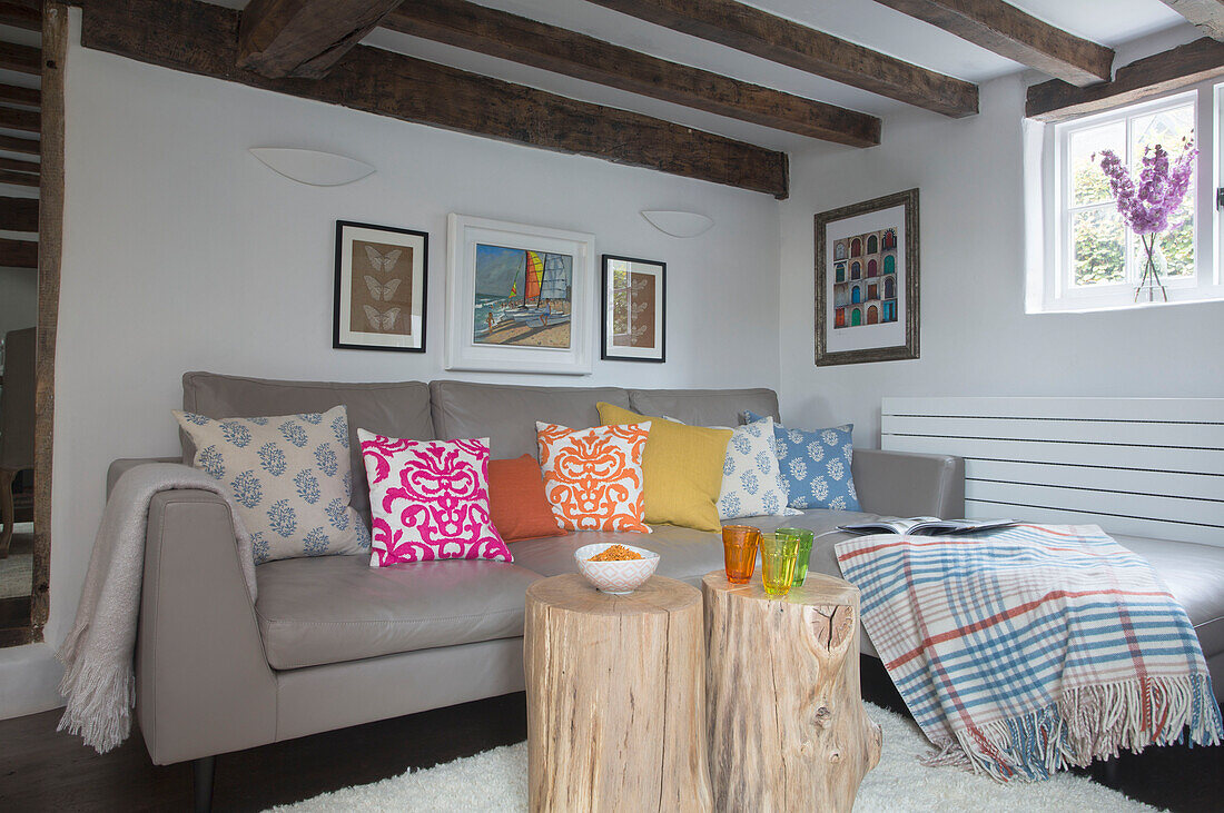 Hölzerne Baumstümpfe und bunte Kissen auf grauem Ledersofa in einem Wohnzimmer mit Balken in Surrey (England)
