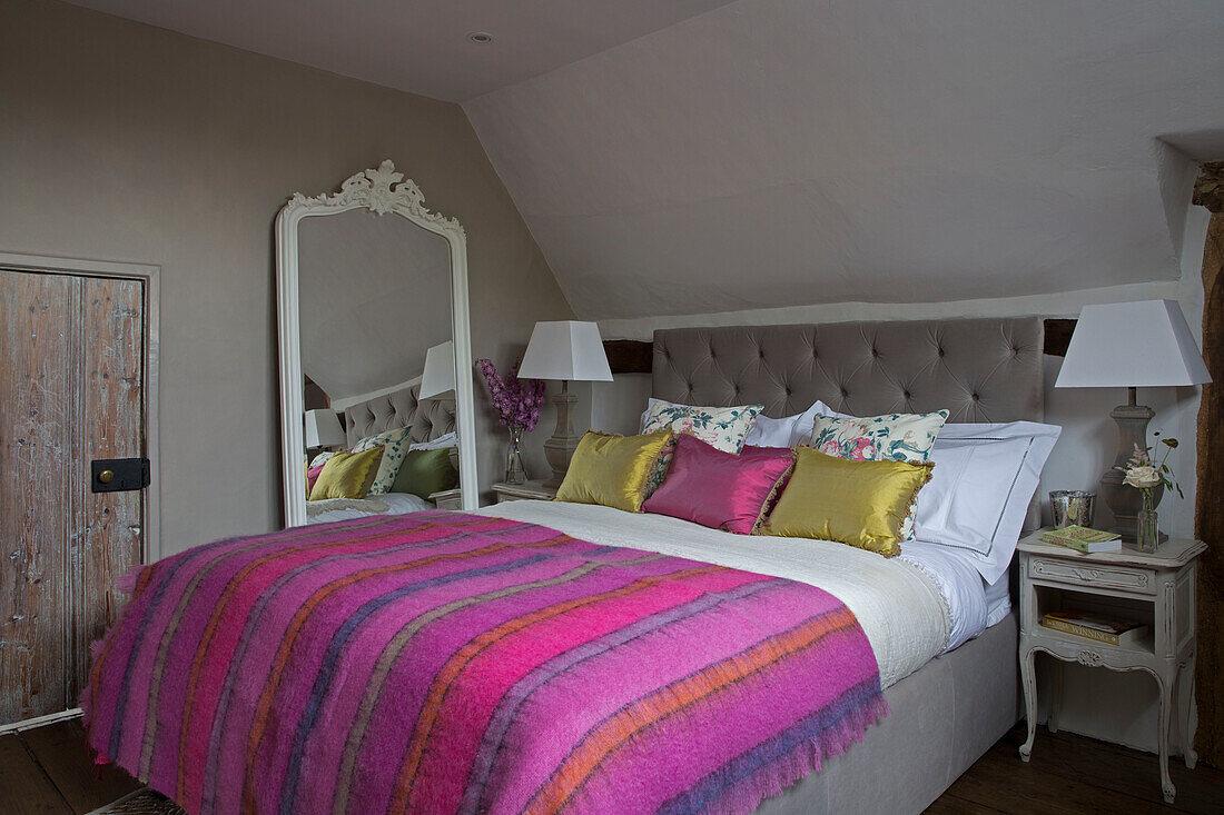 Großer Spiegel neben einem Doppelbett mit hellrosa gestreifter Decke in einem Haus in Surrey, England, UK