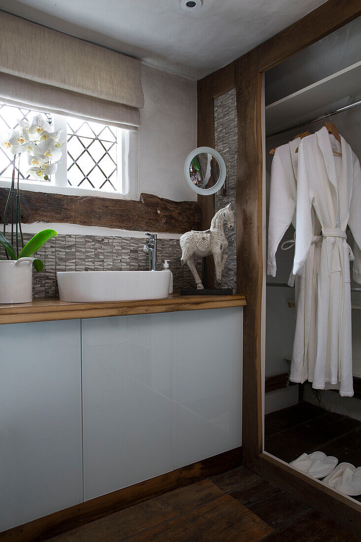 Washbasin below leaded glass window with bathrobe hanging in bathroom of Surrey home England UK