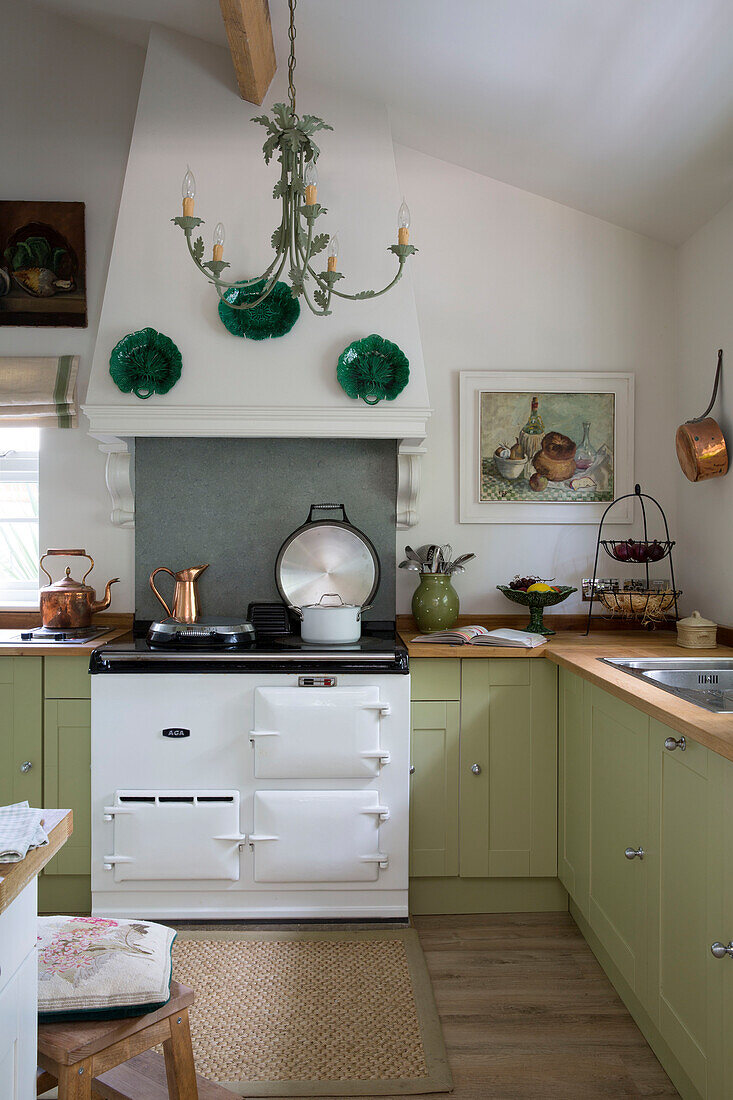 Dekorative Teller und Kupfertöpfe in einer hellgrünen Einbauküche in einem Haus in Dorset England UK