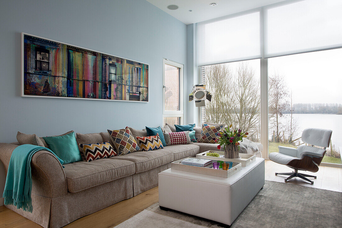Modernes Kunstwerk über einem Sofa mit bodentiefen Fenstern in einem Wohnzimmer in Lechlade, Gloucestershire, England, UK