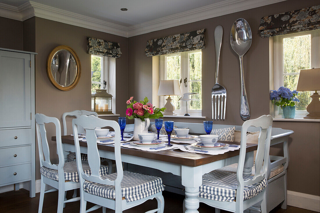 Painted dining chairs with gingham seat covers at table with large spoon and fork in Wokingham cottage Berkshire UK