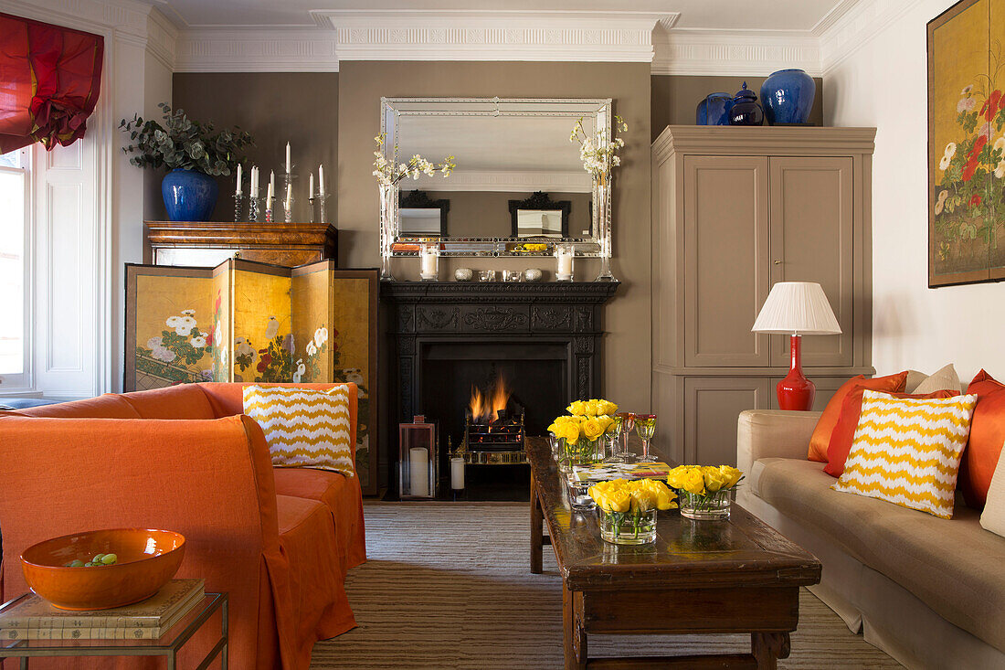 Yellow roses on wooden coffee table with orange sofa in London townhouse living room UK