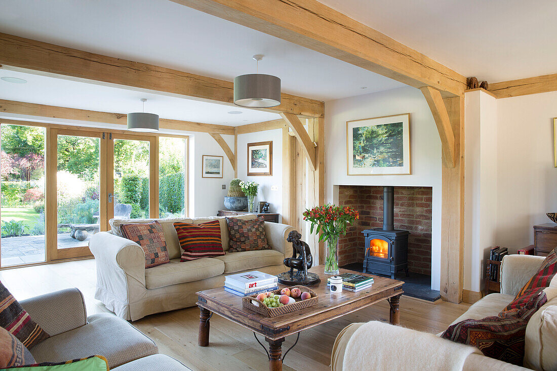 Befeuerter Kaminofen und Sofas mit Couchtisch aus Holz in einem Wohnzimmer in Surrey, England, UK