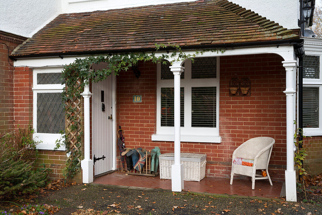 Gummistiefelablage mit Weidenkorb und Stuhl in gemauerter Veranda eines Hauses in Großbritannien