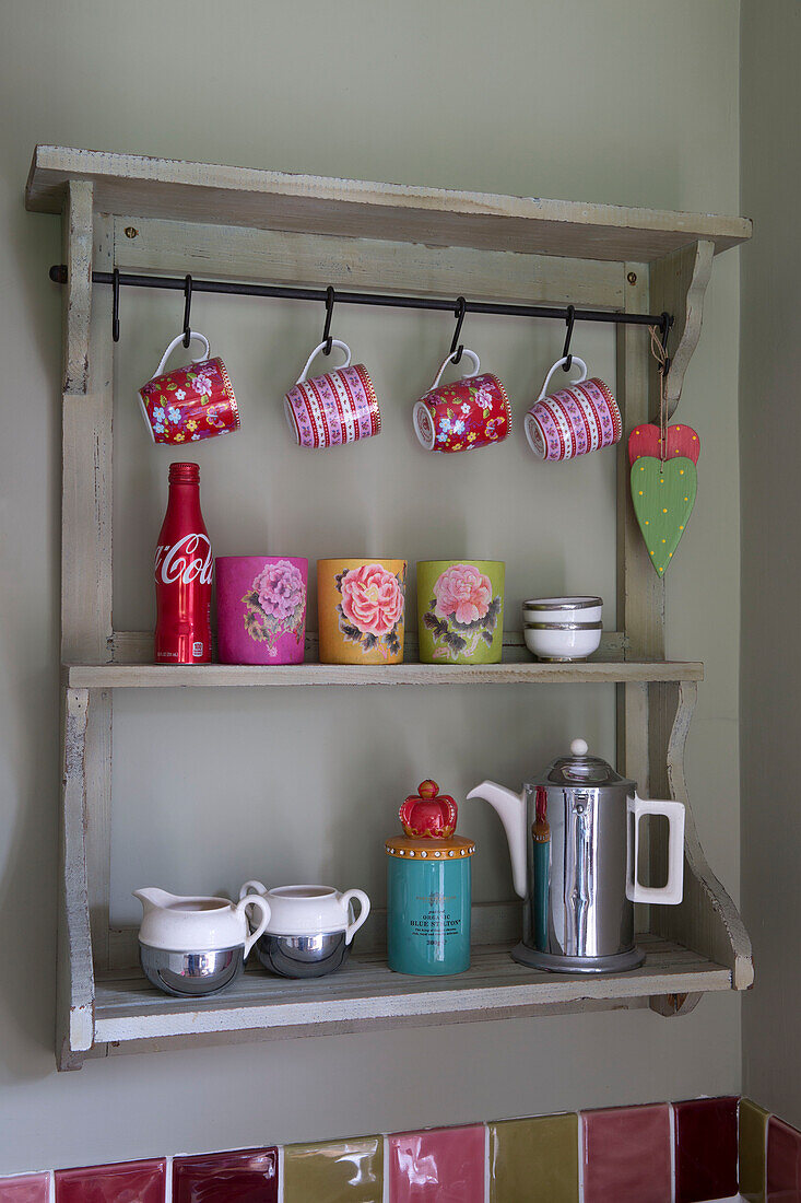 Rote und rosafarbene Tassen mit Kaffeekanne auf Küchenregalen in einem Haus in Großbritannien