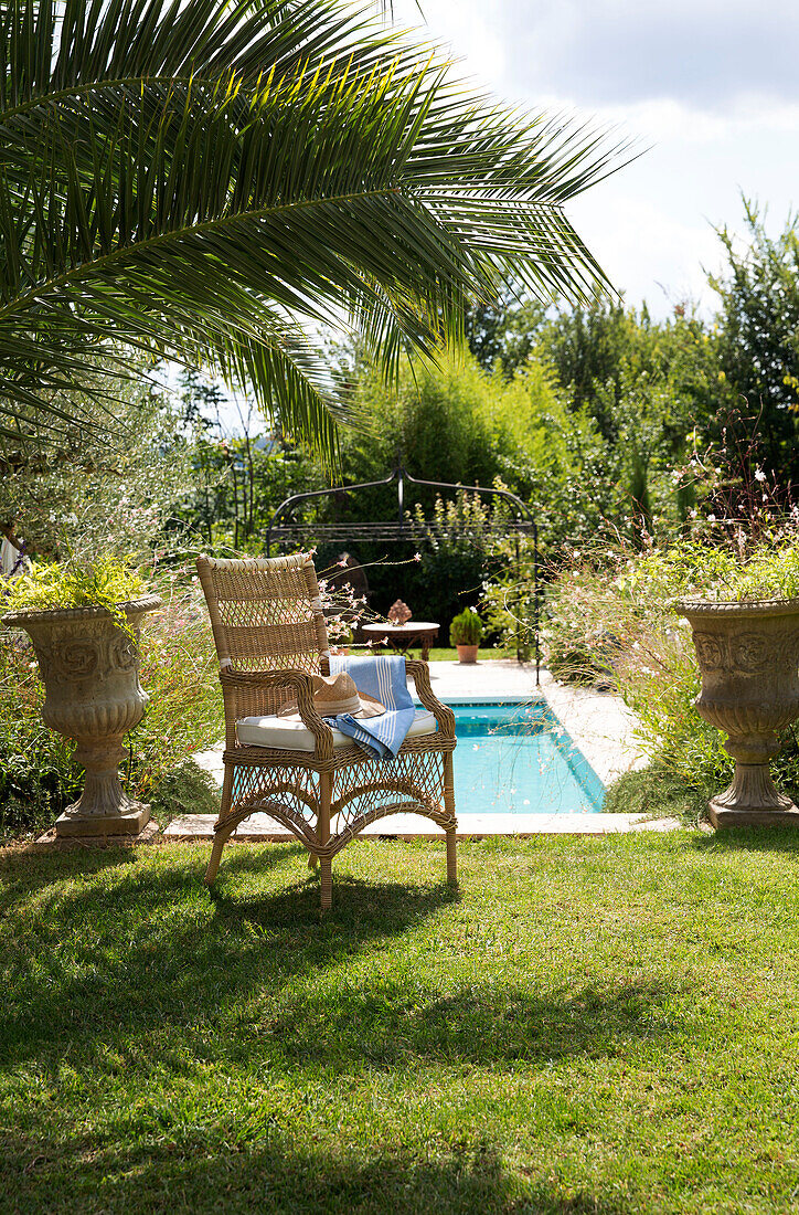 Wicker armchair in shade of palm at poolside in Var Provence France