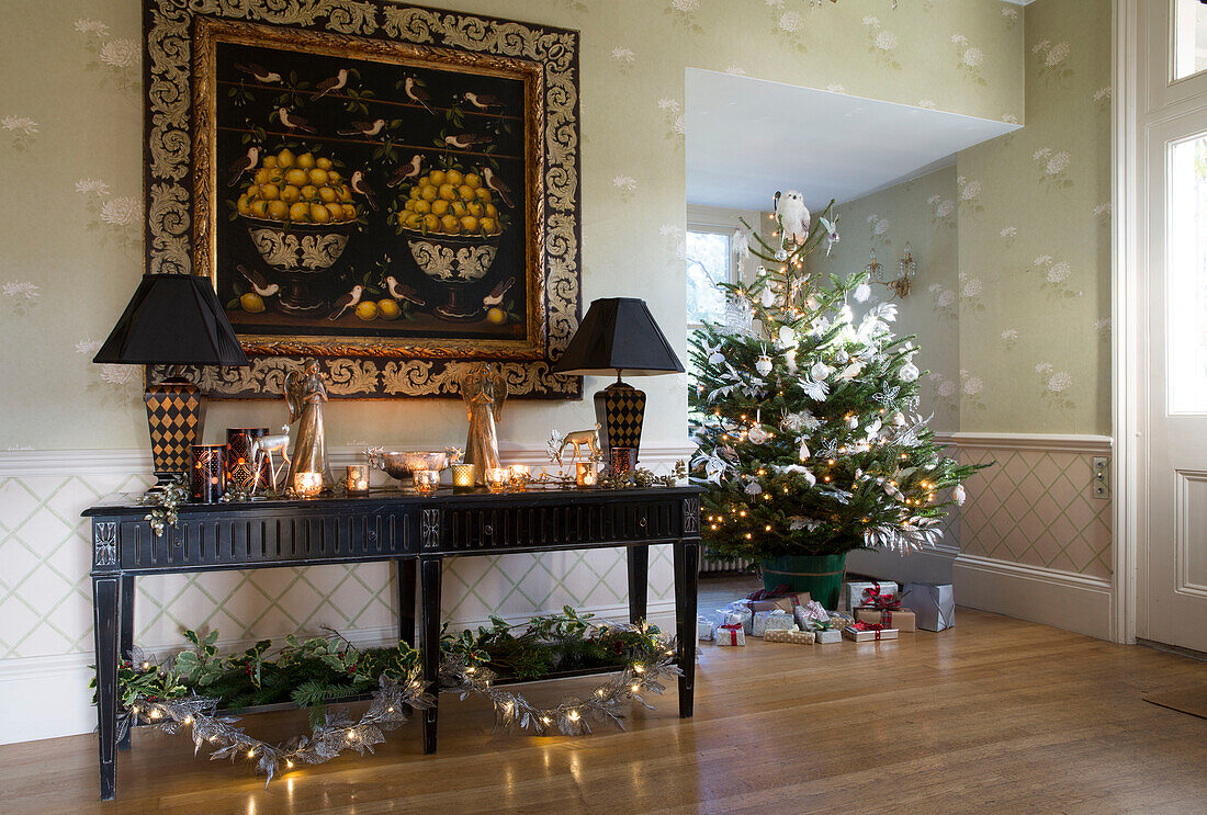 Großes Kunstwerk über der Konsole mit beleuchteten Kerzen und Weihnachtsbaum in einem Haus in Sussex, England, UK