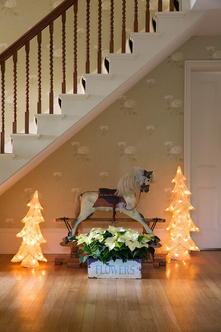 Vintage-Schaukelpferd mit beleuchteten Weihnachtsbäumen und Blumenkasten unter der Treppe in einem Haus in Sussex, England UK