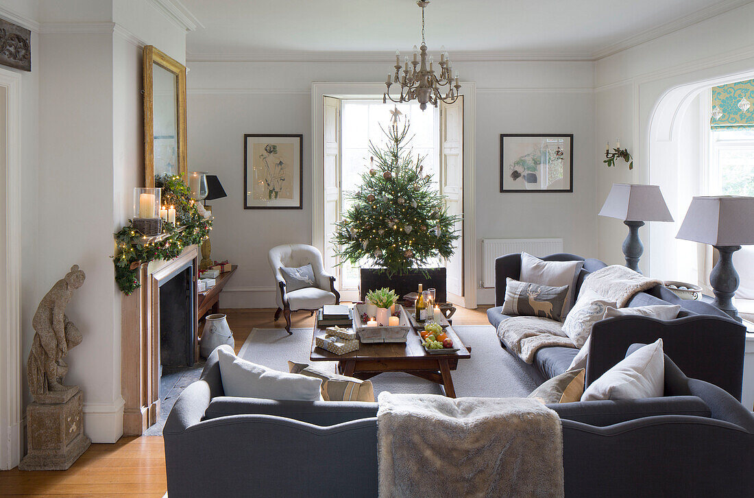 Graue Sofas mit Weihnachtsbaum im Fenster eines Wohnzimmers in Surrey, England UK