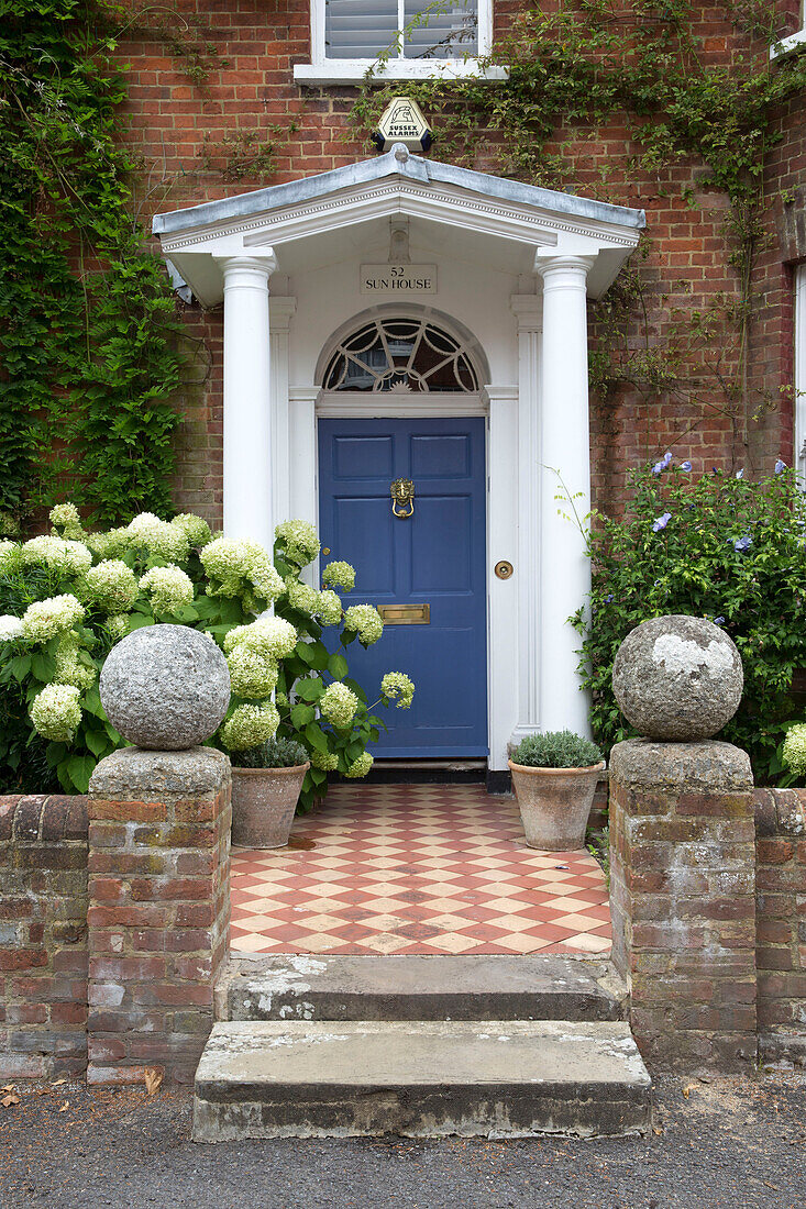 Windfang mit blauer Eingangstür an gefliestem Weg an der Außenseite eines Hauses in Arundel, West Sussex, England, UK
