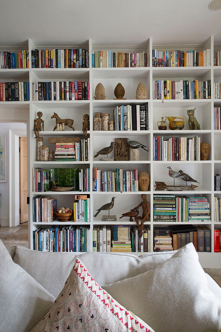 Figuren und Bücher in Regalen im Wohnzimmer eines Hauses in Arundel, West Sussex, England UK