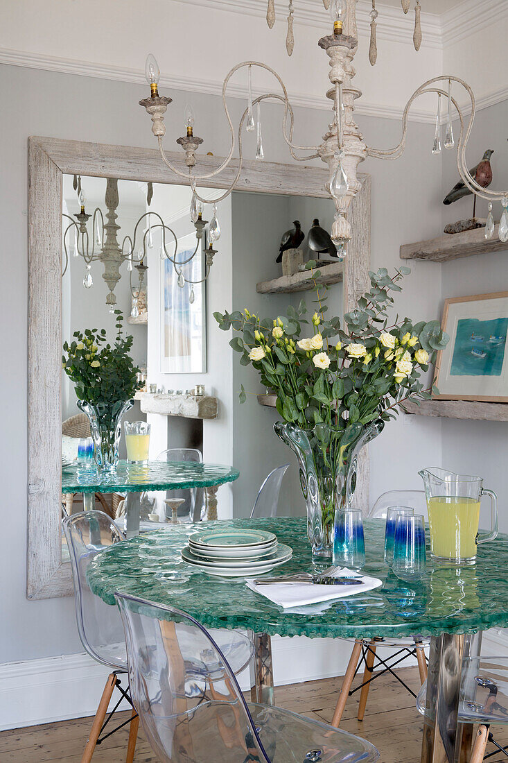 Glas-Esstisch mit Schnittblumen und großem Spiegel in einem Strandhaus in Sussex, England UK