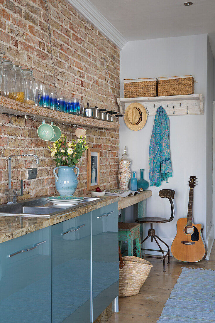 Gitarre und Schreibtisch mit Töpfen auf einem Regal in einer Küche aus Backsteinen in einem Strandhaus in Sussex (England)