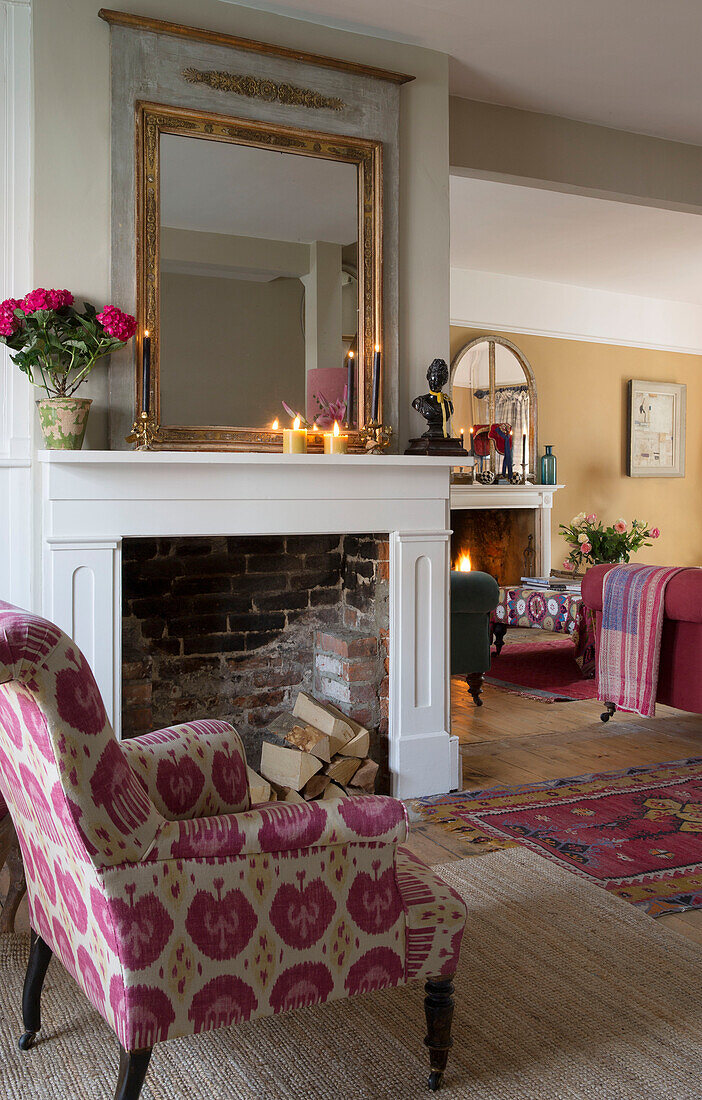 Pink upholstered armchair at fireplace with lit candles in Sussex home England UK