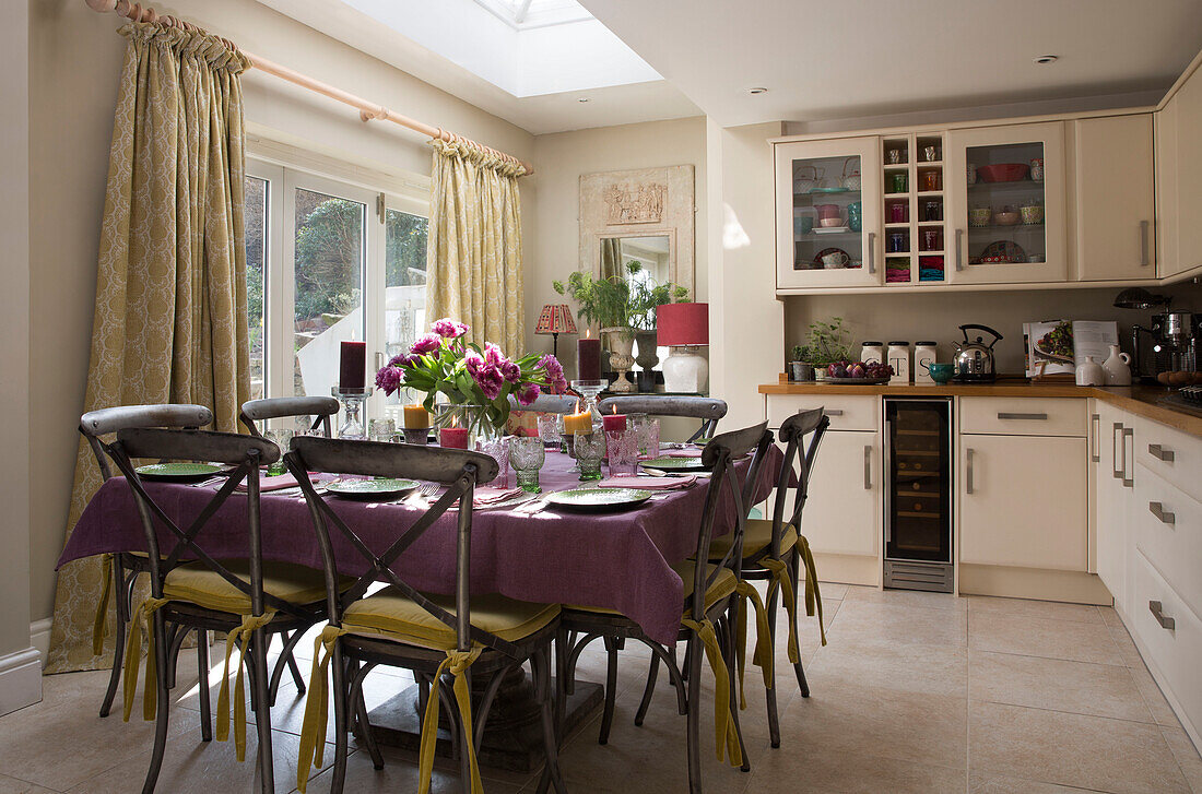 Quadratischer Tisch mit violetter Tischdecke in der sonnenbeschienenen Küche eines Hauses in Sussex England UK