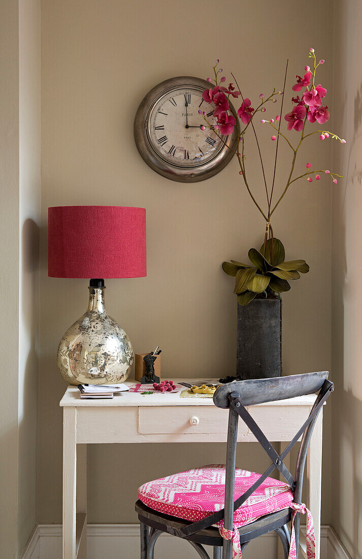 Red lamp and orchid with clock above desk in Sussex home England UK