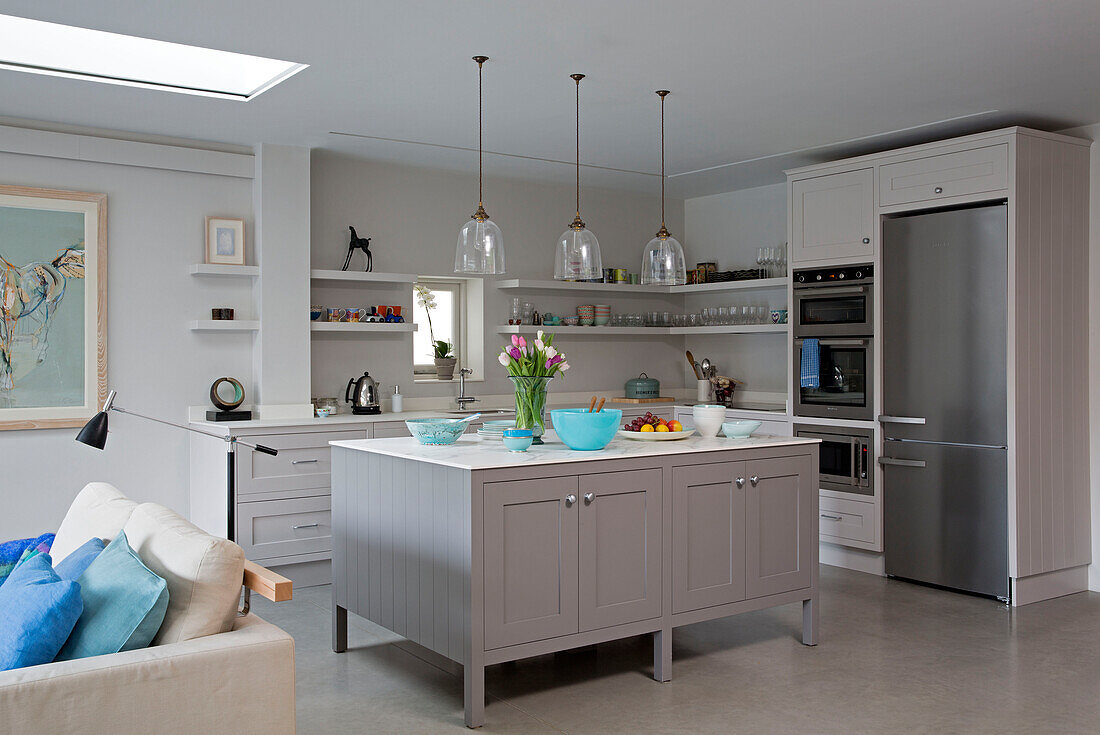 Glass pendant shades above kitchen island with upright fridge in modernised Victorian cottage Sussex England UK