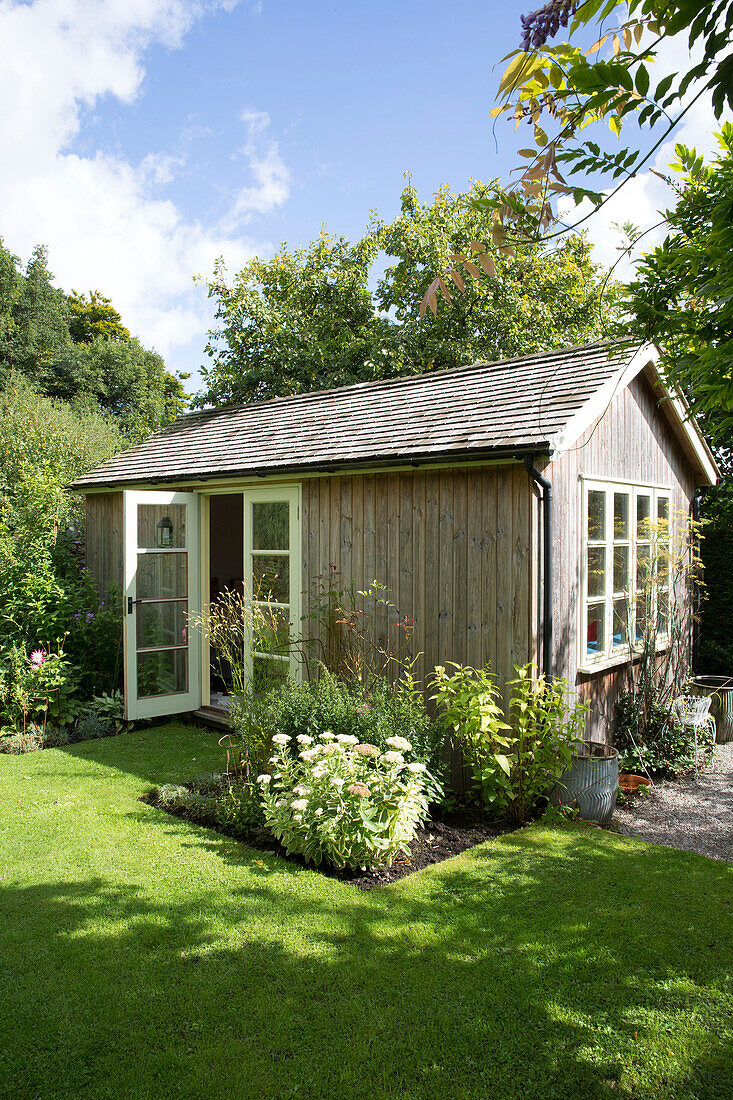 Sonnenbeschienener Rasen mit Gartenhaus für zusätzlichen Lebensraum in einem Garten in Somerset, England, UK