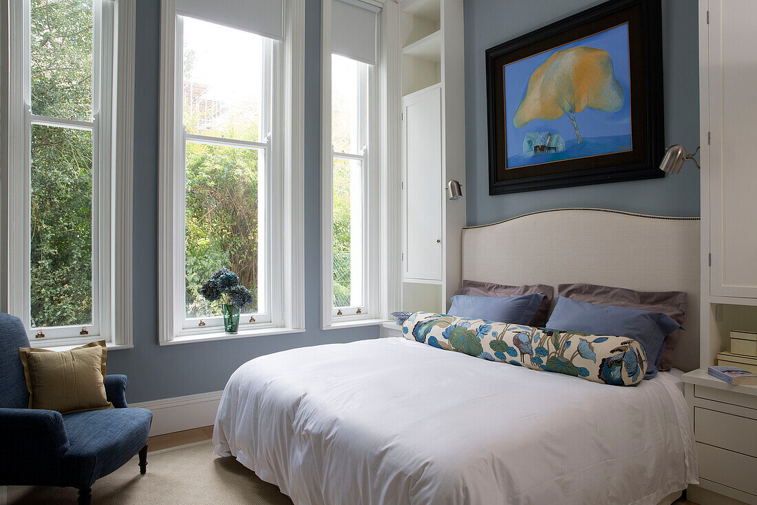 Geblümte Nackenrolle auf einem Doppelbett am Fenster in einem hellblauen Schlafzimmer in einem Londoner Stadthaus UK