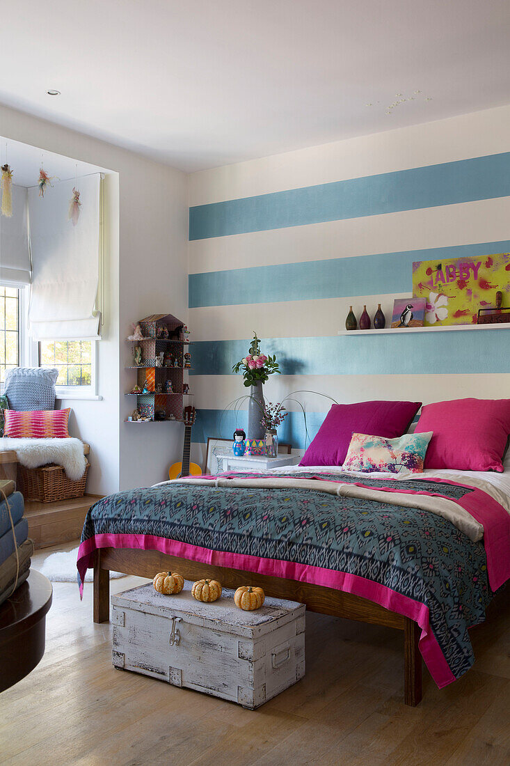 Striped wall above double bed with pink furnishings in London home England UK