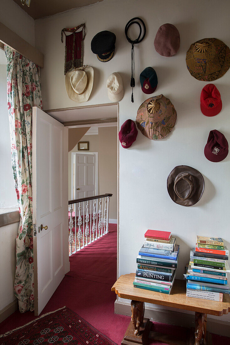Hutsammlung mit gestapelten Büchern auf einem Beistelltisch und rosa Teppich auf dem Treppenabsatz in einem Haus in Kelso, Schottland UK