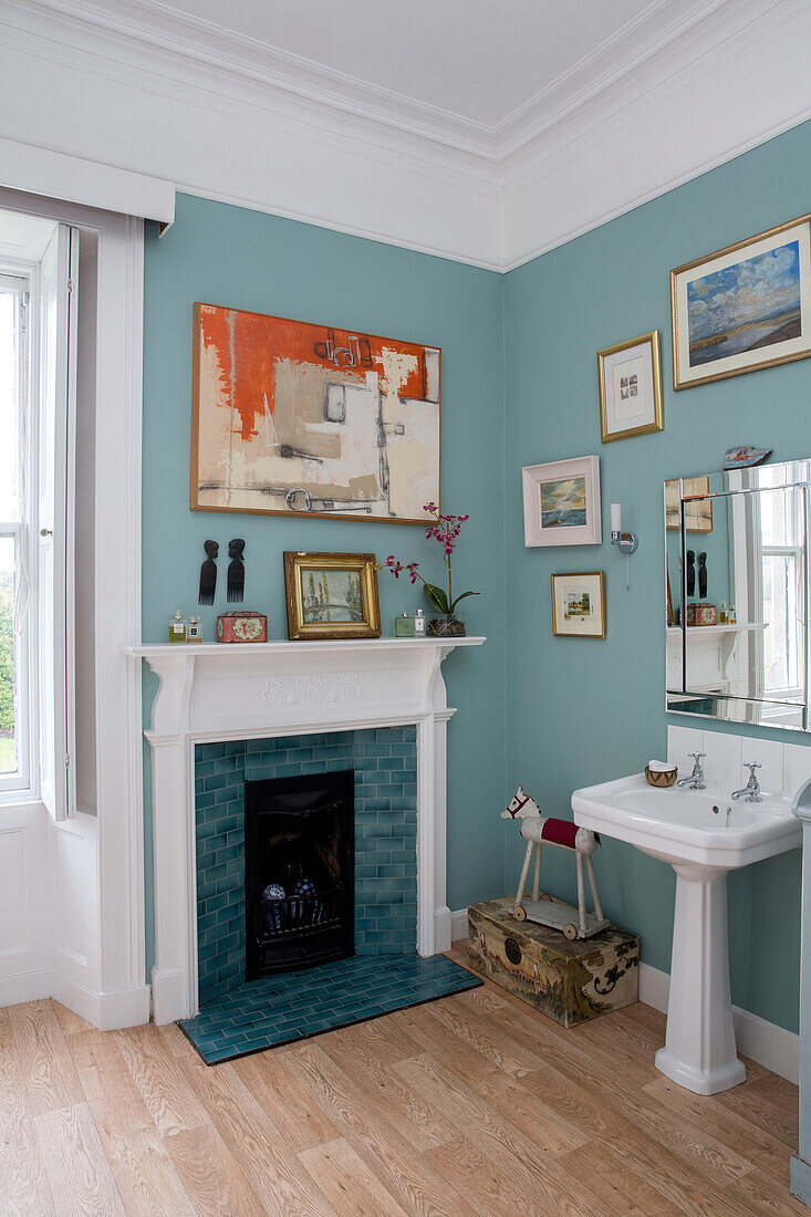 Collection of framed artwork above teal fireplace with pedestal washbasin in Kelso home Scotland UK