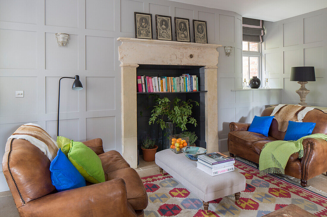 Als Bücherregal umfunktionierter Kamin mit braunen Ledersofas in einem Wohnzimmer in Gloucestershire (England)