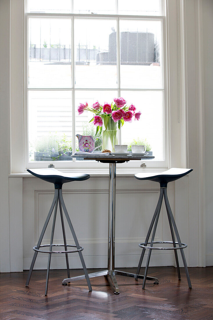 Pink Peonies (Paeonia) and bar stools in at window in London townhouse England UK