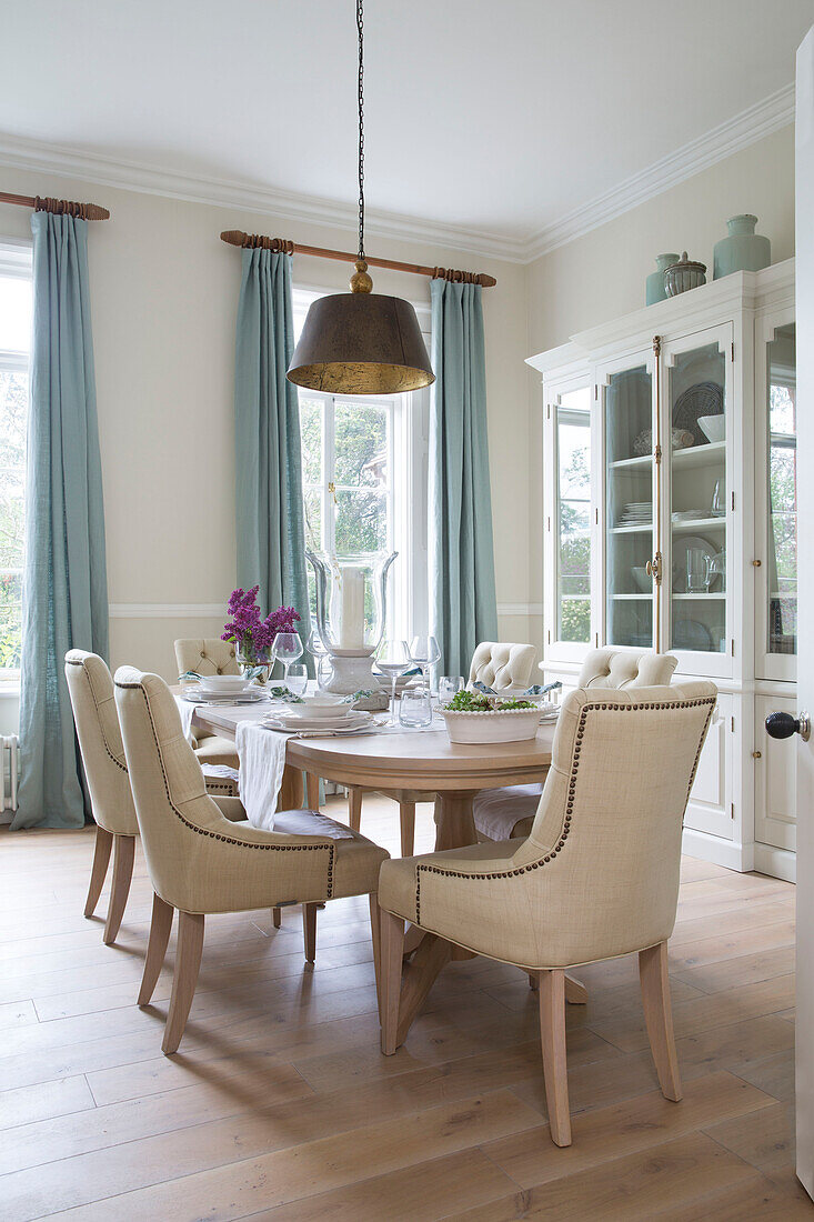 Light blue curtains with glass fronted cabinet and dining table and chairs in Worcestershire home England UK