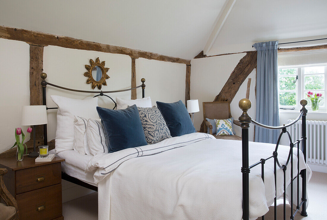 Sunburst-Spiegel über einem Bett mit Metallrahmen und blauen Samtkissen in einem Bauernhaus mit Holzrahmen in Worcestershire England UK