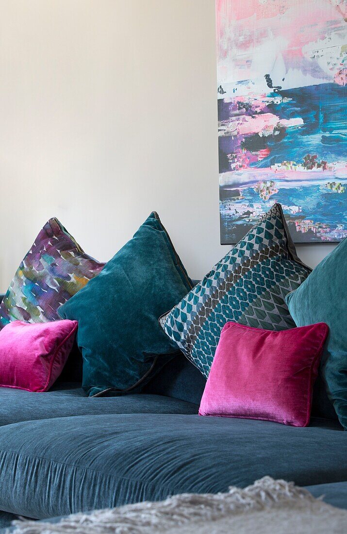 Rosa und blaugrüne Kissen mit moderner Kunst über dem Sofa in einem Haus in Sussex (England)