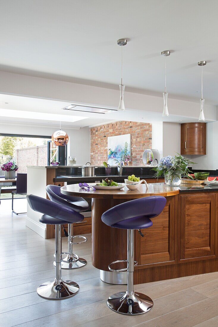 Purple leather bar stools at wooden kitchen island in open plan Sussex home England UK