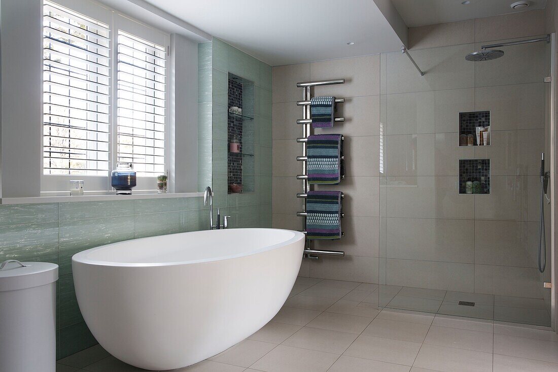 Freestanding bath under window with Venetian blinds and wall mounted towel rack in Sussex home England UK