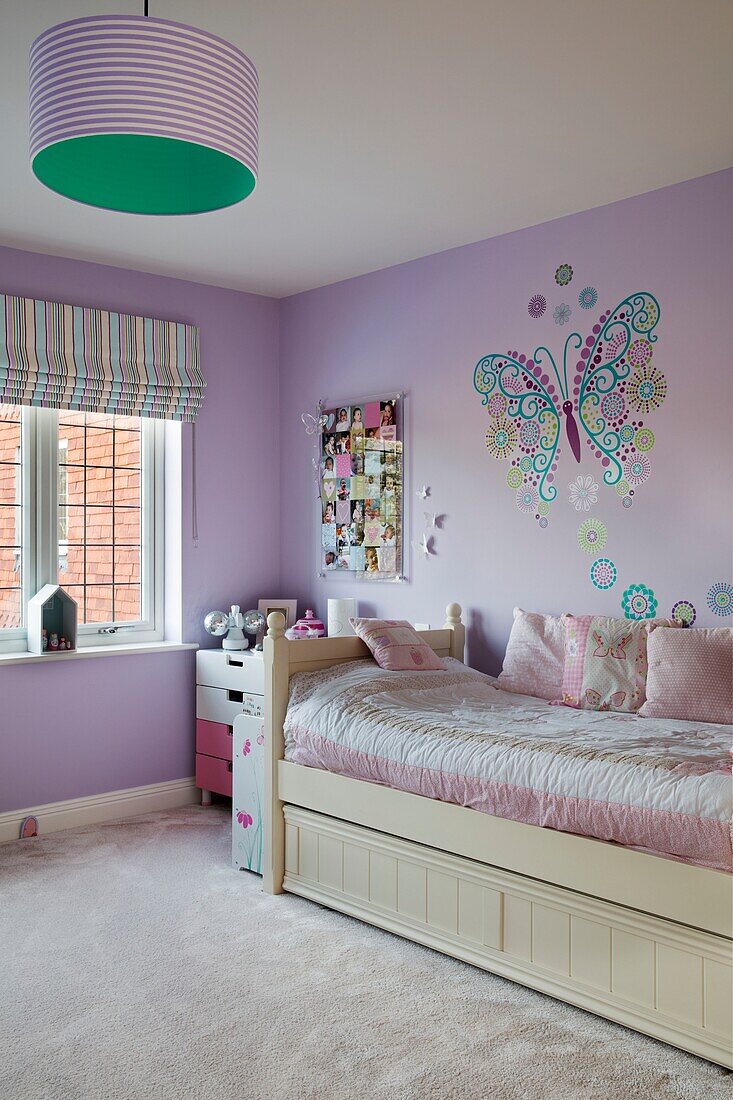 Schmetterling Wanddekoration über Einzelbett mit rosa Bettdecke in fliederfarbenem Schlafzimmer in einem Haus in Sussex, England, UK