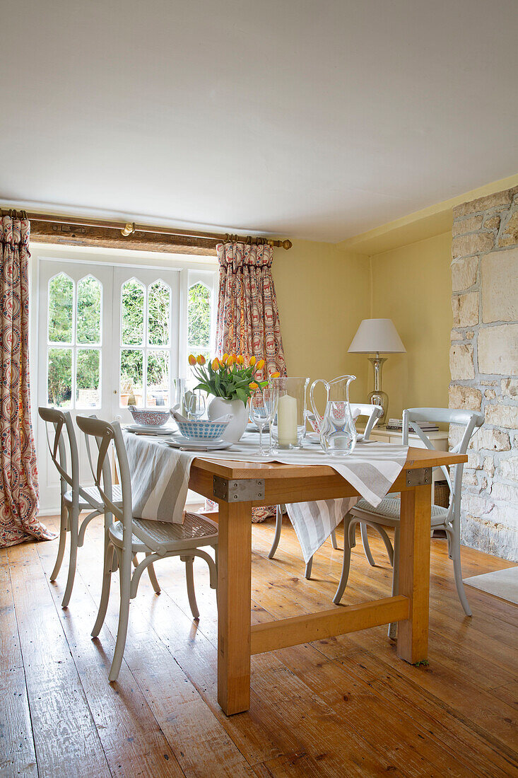 Painted chairs at wooden dining table in Gloucestershire farmhouse England UK